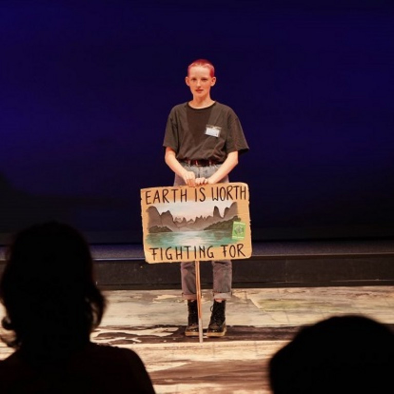 Bild von einer weiblichen Person. Vor sich ein Schild auf dem steht: Earth is worth fighting for! (Übersetzung: Die Erde ist es wert, gerettet zu werden!)