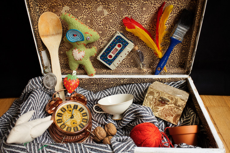 Ein Koffer mit vielen verschiedenen Gegenständern, unter anderem: Kochlöffel, Wecker, Kasette, Teetasse, Pinsel, Blumentopf, Wallnüsse etc. 