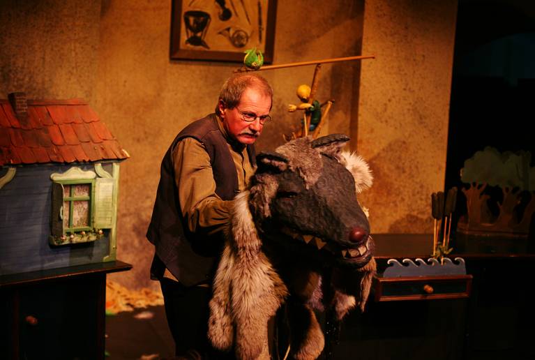 Inszenierungsfoto, in dem der Puppenspieler Wilfried Reach die Figur des Wolfs vor sich hält. 