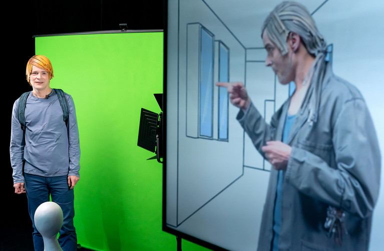 Schauspieler Sven Reese links im Bild vor einem Greenscreen. Rechts im Bild ein großer Bildschirm, in dem Sven Reese in einer anderen Kostümierung in einer gezeichneten Umgebung zu sehen ist.
